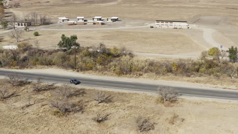 drone shot of road in the countryside with wide meadow, seen cars passing