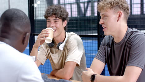 young diverse men enjoying conversation and coffee after playing padel tennis on indoor court