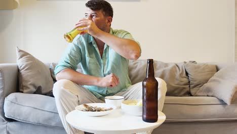 man relaxing on a couch, drinking beer and eating snacks