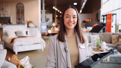 una joven madre profesional formal mujer gerente de empresa ventas mujer de negocios camina hacia la cámara riendo sonriendo mirando hacia abajo feliz en su trabajo ipad tableta dispositivo dentro de una tienda de muebles