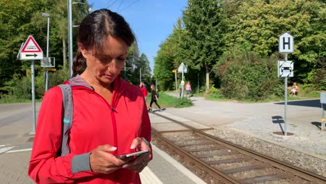 mujer mayor deportiva mirando su teléfono mientras espera el tren frente a la cámara