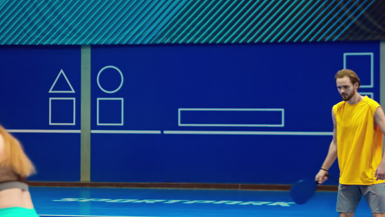 A man and a woman playing pickleball on a blue, inside court