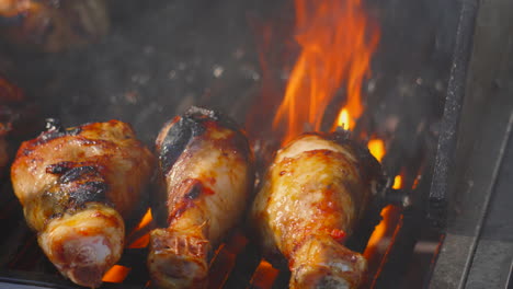 trio of chicken drumsticks cooking on hot flames of bbq in bright sunlight. summer food being cooked outside. high quality prores footage.