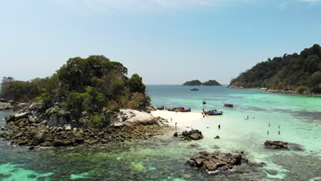 Aerial-view-of-a-small-island-on-a-paradisiac-place-with-groups-of-people-enjoying-the-beach