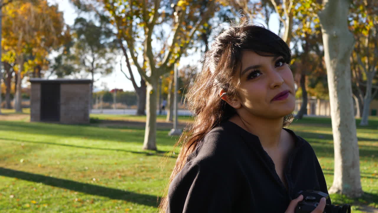 una linda modelo de chica en un soleado parque de hierba con hojas de otoño en los árboles mirando a la cámara en cámara lenta