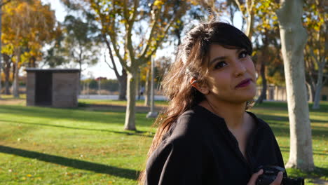 una linda modelo de chica en un soleado parque de hierba con hojas de otoño en los árboles mirando a la cámara en cámara lenta