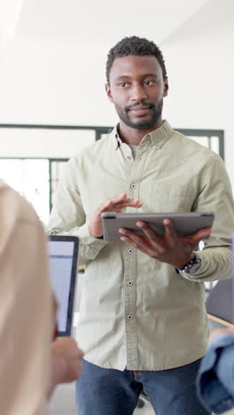 vertical video of happy diverse business people with tablet talking in office