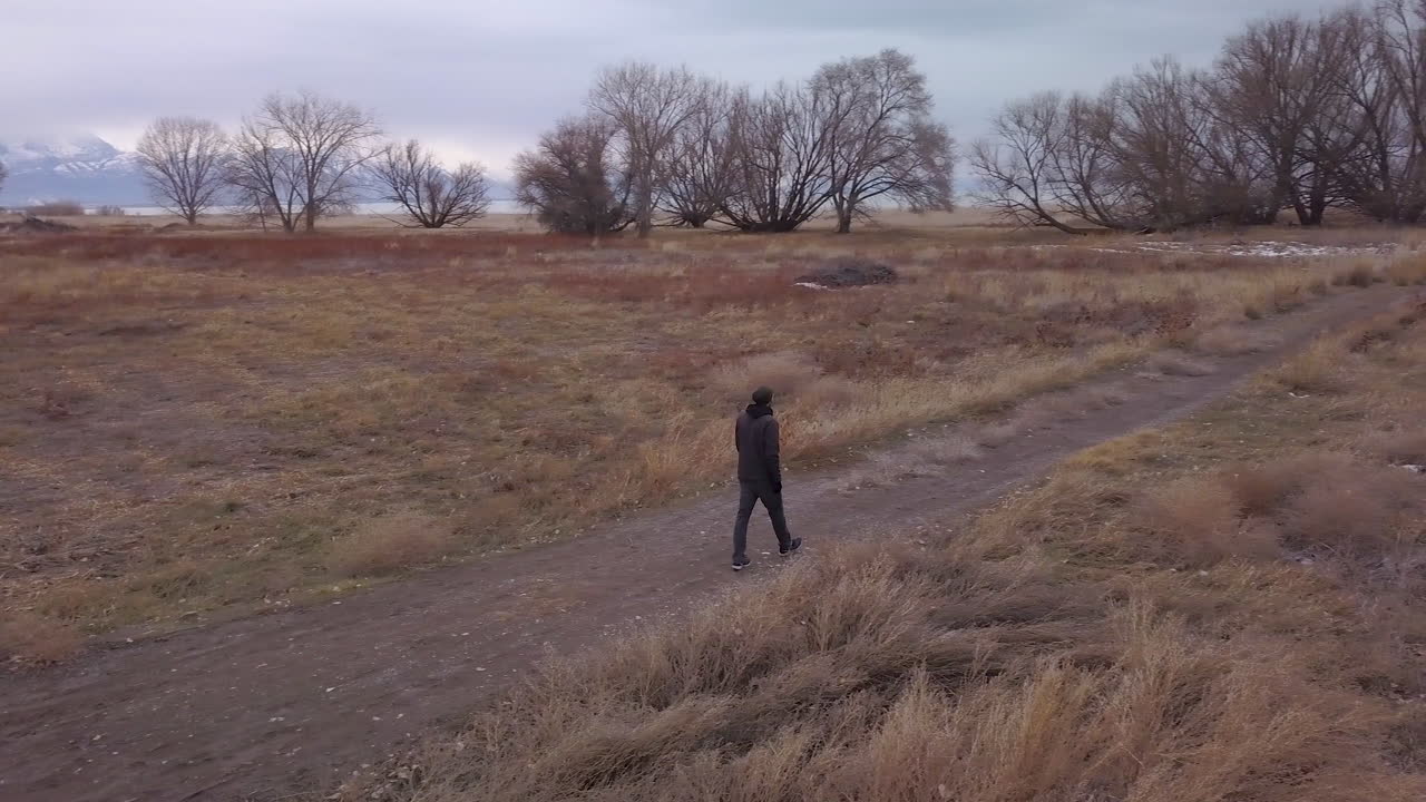 un hombre camina fuera del camino pavimentado hacia un lago y montañas - panorámica y zoom