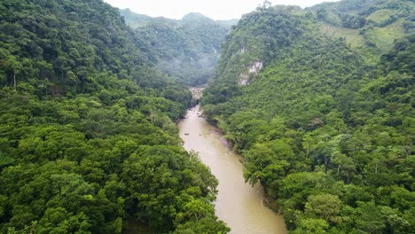 drone aerial panorama of flowing rainforest river valley lined with lush green trees surrounded by dense jungle hillsides and mountains