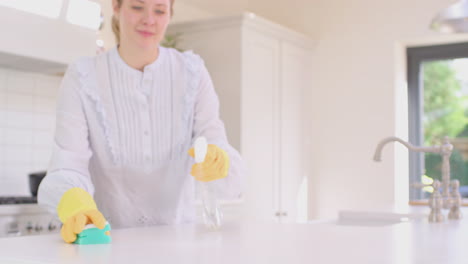 woman at home in kitchen wearing rubber gloves cleaning down work surface using cleaning spray - shot in slow motion