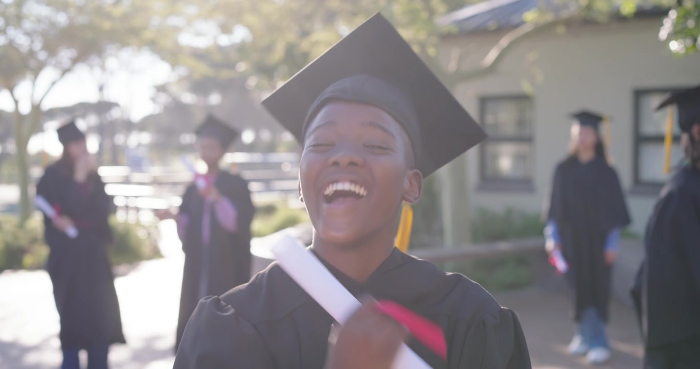 Laureata afroamericana che ride dopo la laurea nel campus, tenendo il tocco e un diploma con nastro rosso