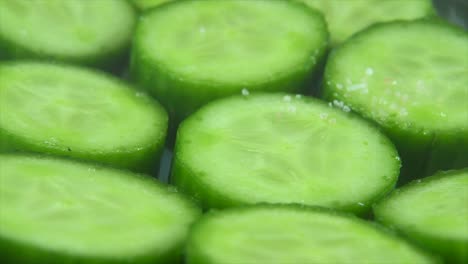 A-macro-close-up-shot,-falling-salt-grains-on-a-cut-slices-of-a-fresh-green-cucumber,-slow-motion-4K-video