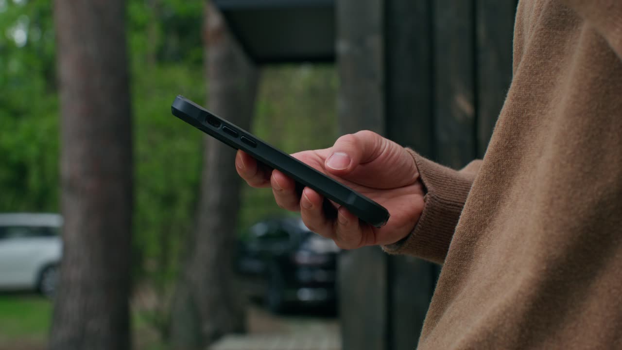 Person bruger en smartphone udendørs nær en hytte