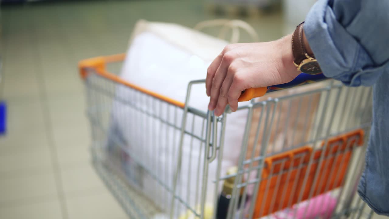 Close up of a woman's hands holding and pushing a trolley with goods in the supermarket. Backside view