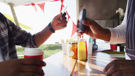 sección media de un hombre afroamericano pagando al dueño masculino por café con tarjeta de crédito en un camión de comida
