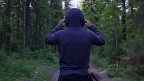 person in a hoodie walking through a forest