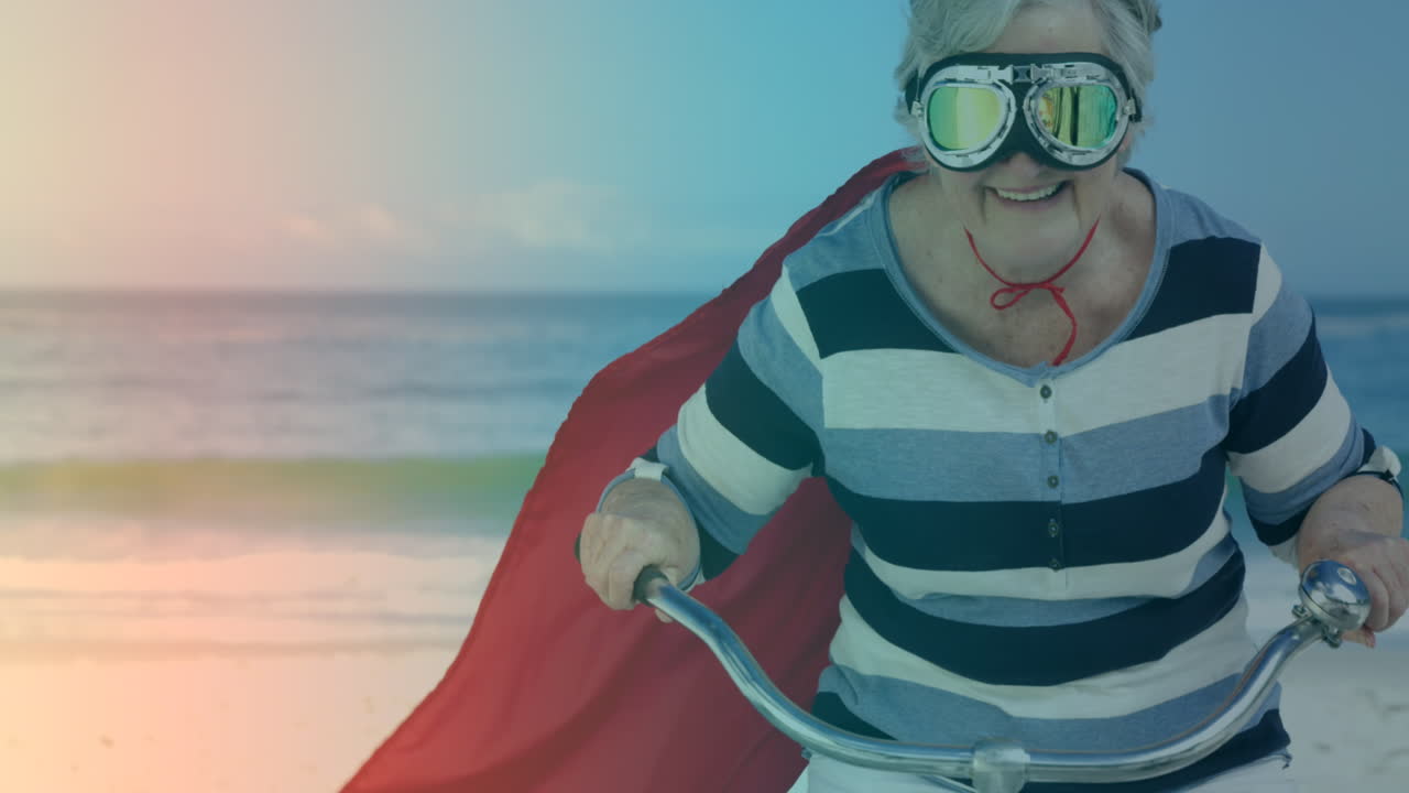 해변에서 자전거를 타고 슈퍼히어로 의상을 입은 백인 고령 여성에 대한 빛의 반점