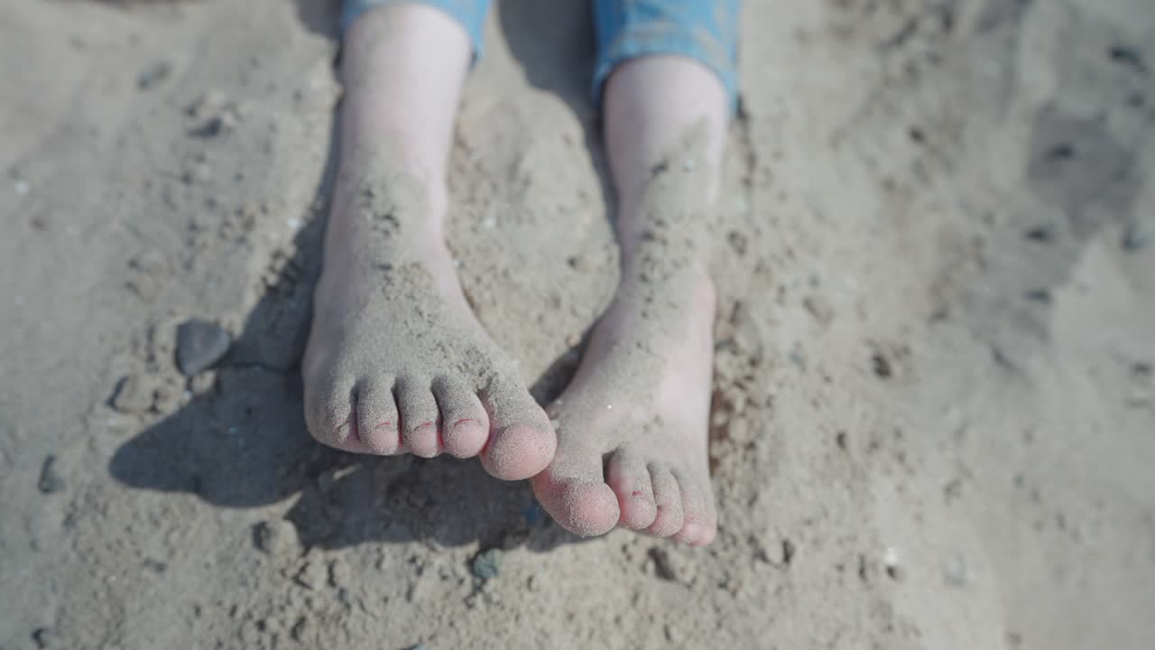 Teenage girl sitting on the beach throwing sand over her feet, closeup