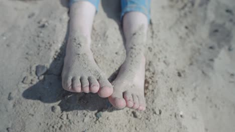 teenage girl sitting on the beach throwing sand over her feet, closeup