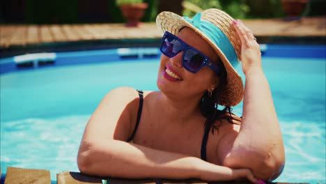 woman enjoying summer day by swimming pool, wearing sunglasses and straw hat, relaxing outdoors