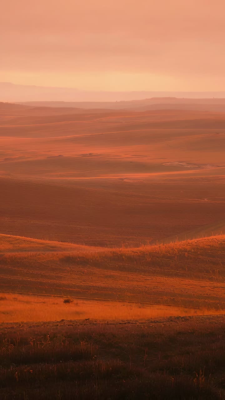 Vertical video: Gliding aerial camera showing rolling terrain at dawn, with layered ridges and haze