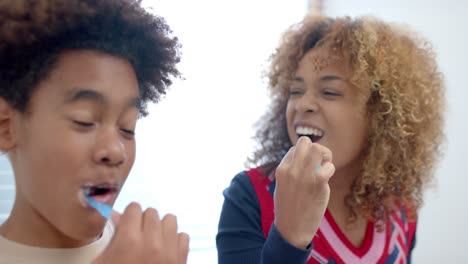 Happy-african-american-mother-and-son-brushing-teeth-in-bathroom,-slow-motion