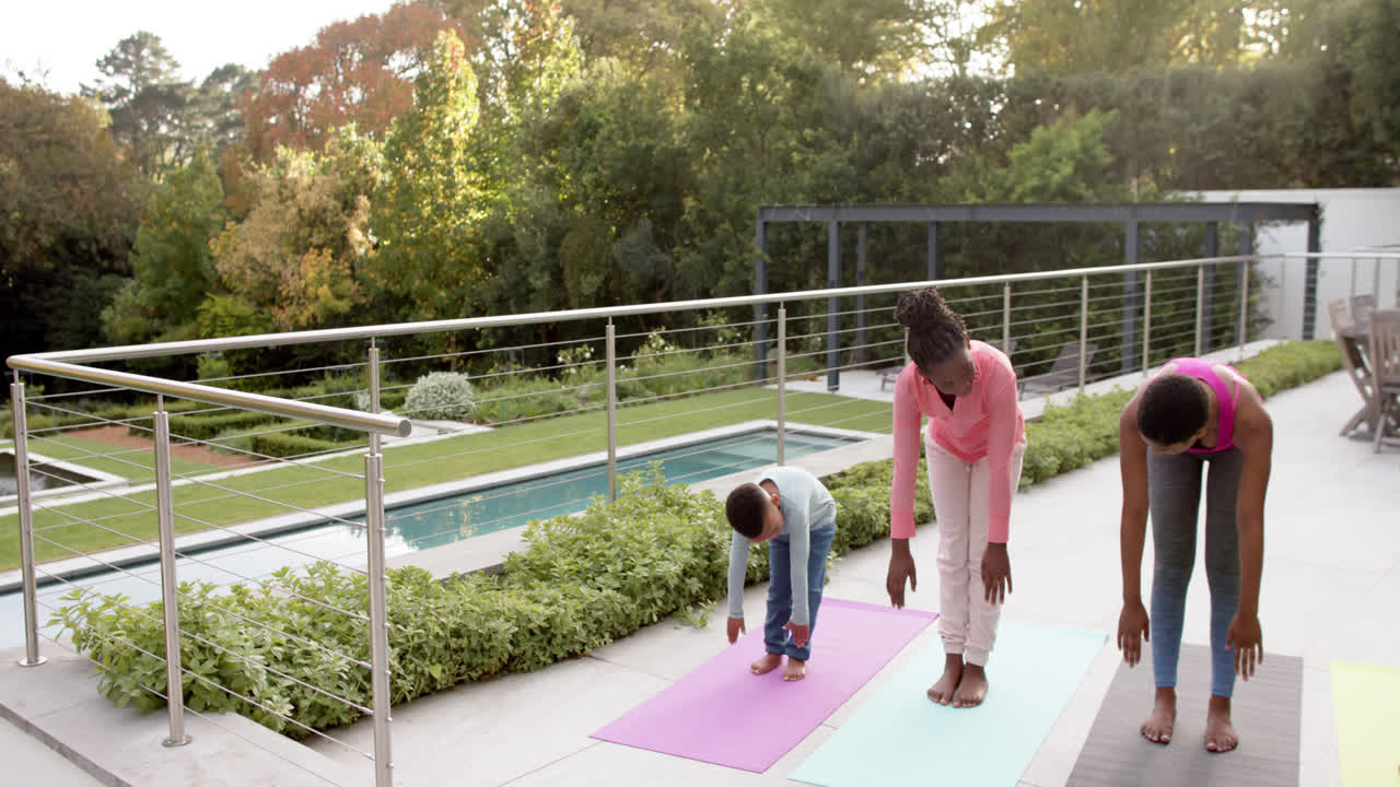 felices padres afroamericanos, hijo e hija practicando yoga en un jardín soleado, en cámara lenta.