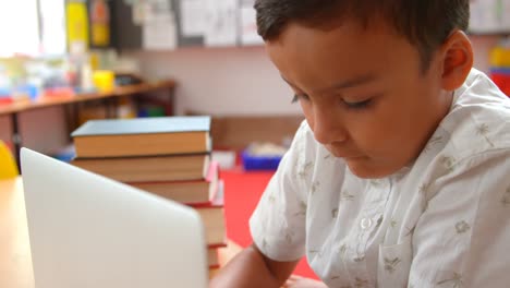 Front-view-of-attentive-Asian-schoolboy-studying-with-laptop-in-a-classroom-at-school-4k