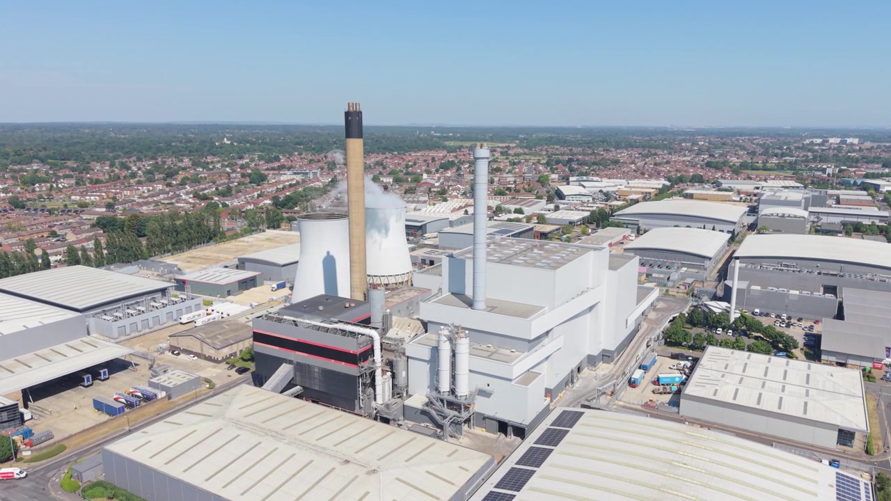 Una prospettiva aerea mostra una centrale elettrica multi-combustibile da rifiuti a energia che opera in un'area industriale. Il vapore sale dalle strutture sotto un cielo azzurro e limpido in una giornata luminosa. L'impianto genera energia