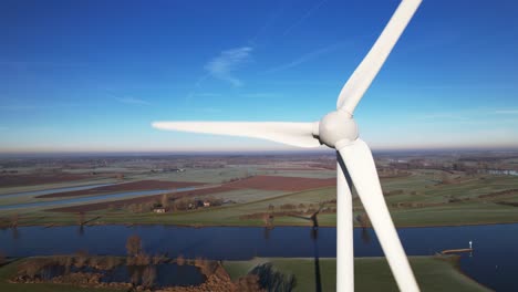 Single-wind-mill-turbine-seen-from-up-close-with-blades-rotating-in-The-Netherlands-part-of-sustainable-industry-in-Dutch-landscape-river-IJssel-and-Twentekanaal-meet