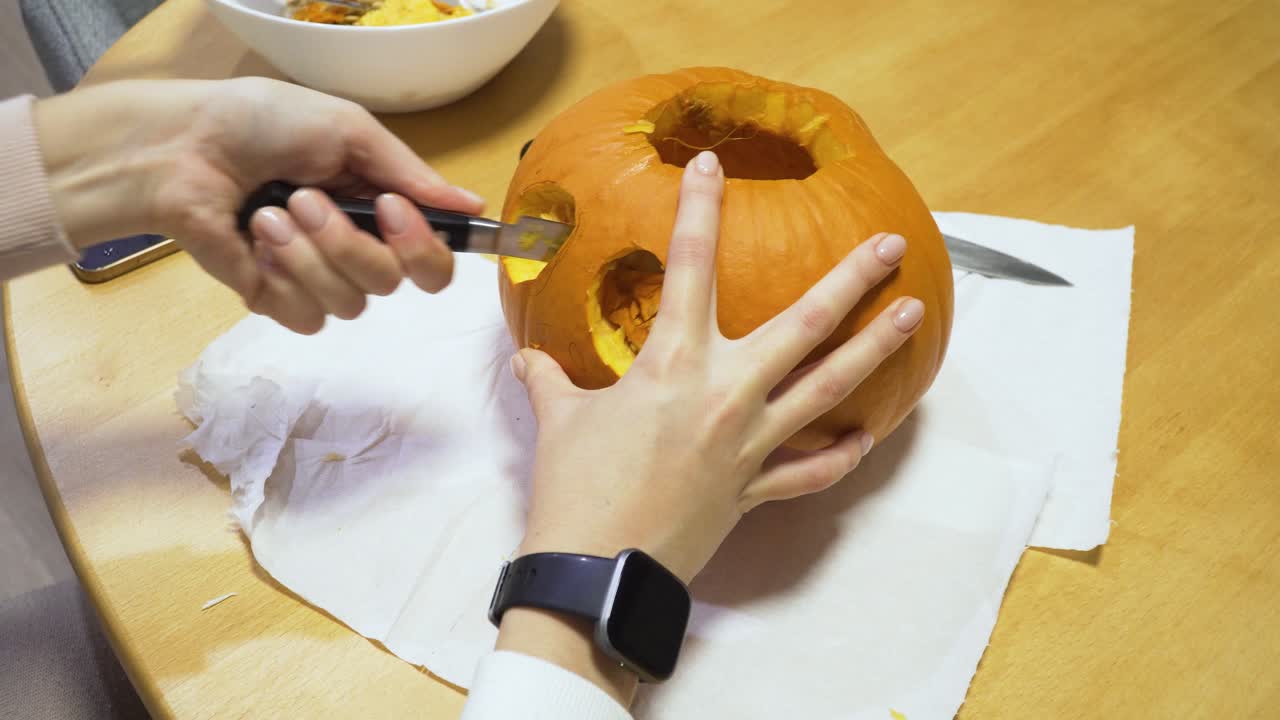 4k에서 할로윈을 위해 집에서 주황색 호박을 조각하는 여성의 클로즈업 샷