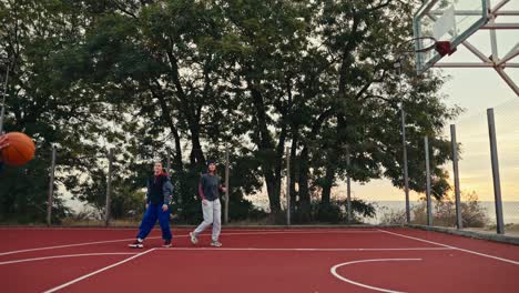 A-blonde-girl-in-a-turquoise-hoodie-and-sportswear-plays-basketball-on-the-Red-street-court-with-her-friends-in-the-morning-in-the-summer.-Blonde-girl-and-her-friends-play-basketball-in-the-morning-in-the-summer