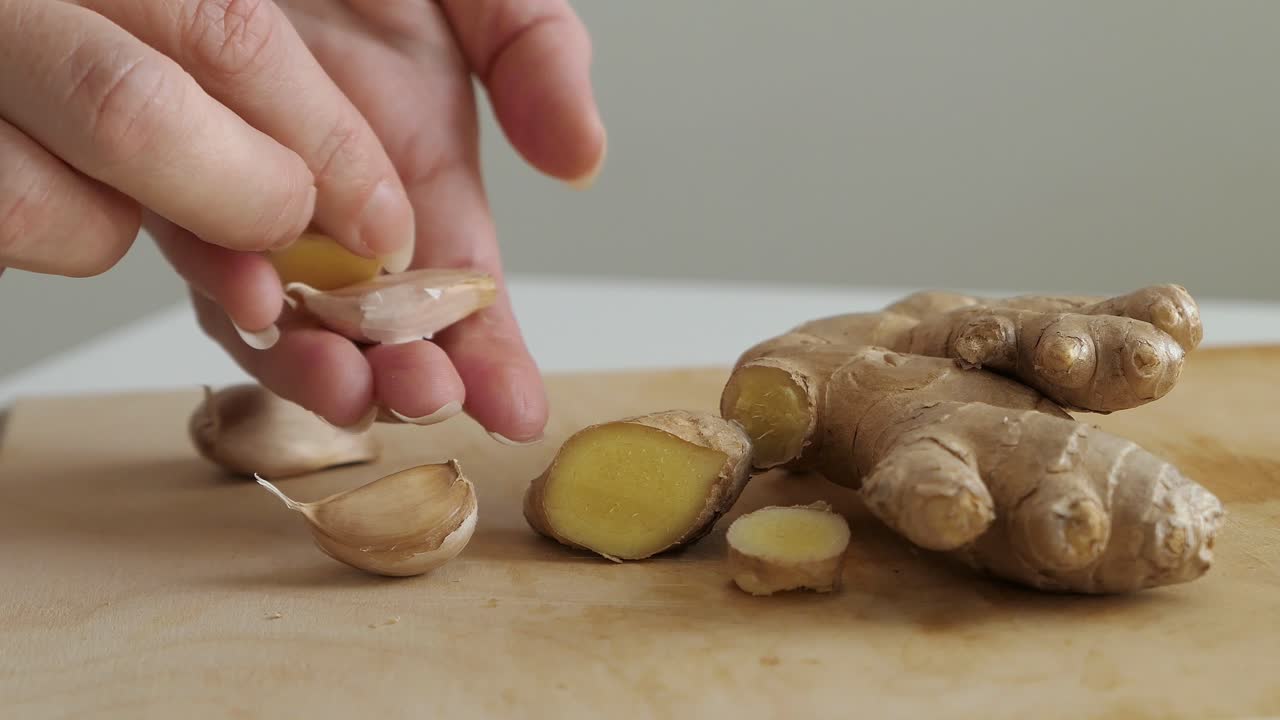Woman picking up fresh ginger and garlic off wooden cutting board, healthy eating close up