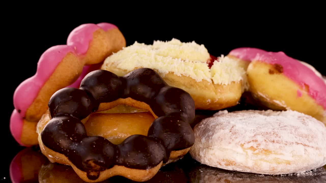 Rotating assortment of chocolate, strawberry, and powdered donuts on reflective surface with dramatic lighting