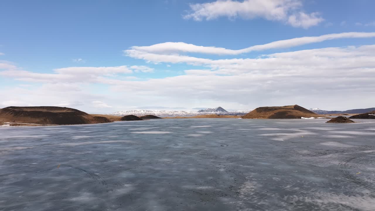 Frozen lake Mývatn with surrounding pseudo craters near Skútustaðir and Reykjahlíð, Iceland, under a bright blue sky with scattered clouds, showcasing Arctic volcanic tranquility.
