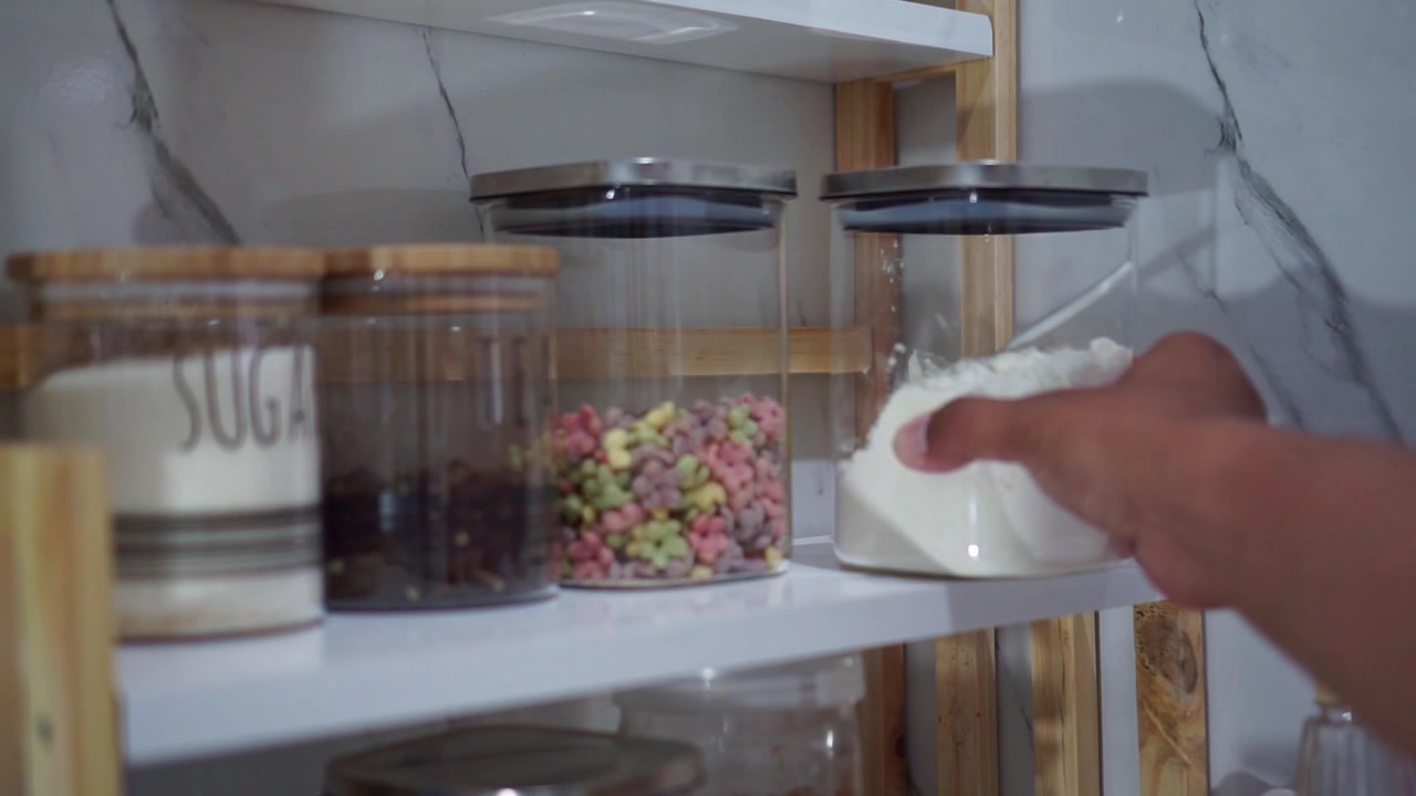 Mano che posiziona un barattolo di farina bianca su uno scaffale, contenitori da cucina organizzati, concetto di organizzazione della dispensa.