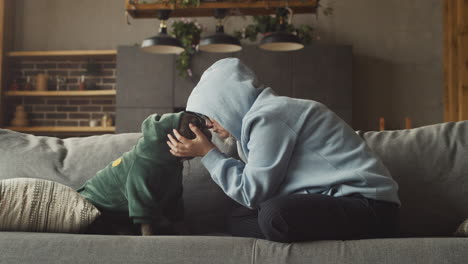 Red-Haired-Woman-Puts-A-Hood-On-Her-Bulldog-Dog-Head-And-Caresses-Her-While-Sitting-On-The-Couch-In-The-Living-Room-At-Home-1