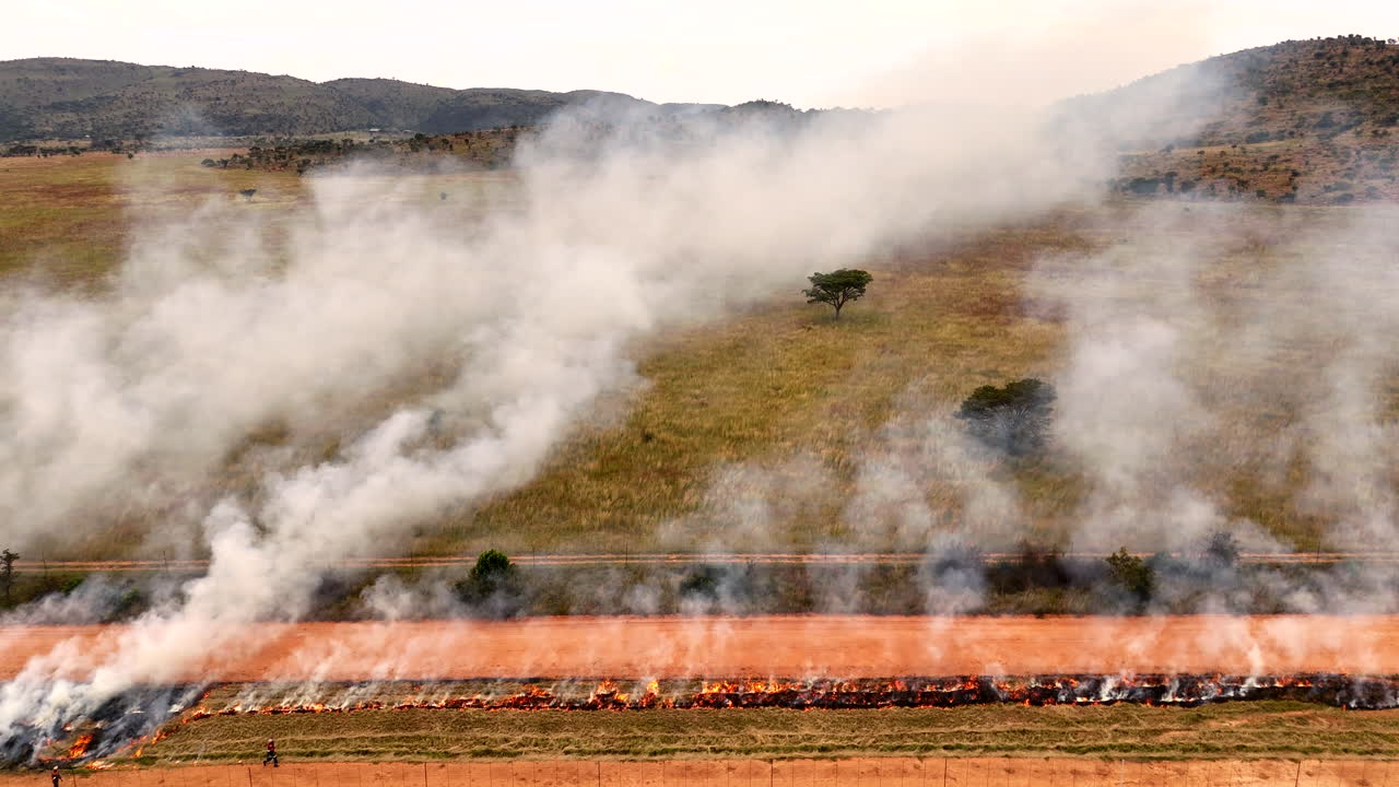 Aerial view of farmworkers burning dry grass along district road for safety