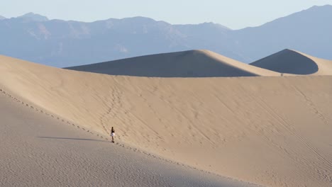 woman walking up on steep sand dune in death valley national park in california, usa - slow motion