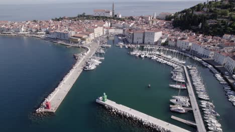 Anschauliches-Schwenkdrohnenvideo-über-Die-Stadt-Piran-In-Slowenien,-Man-Sieht-Den-Hafen-Mit-Den-Booten-Im-Wasser-Als-Hauptteil-Und-Die-Kirche-Im-Hintergrund