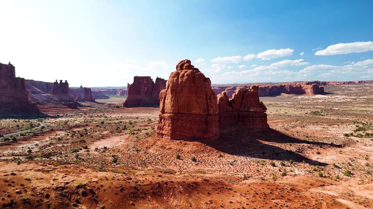 Splendido filmato stock del Parco Nazionale di Arches, USA, durante un pomeriggio luminoso. La luce solare brillante illumina le maestose strutture di arenaria rossa e il paesaggio desertico sotto un cielo azzurro limpido.
