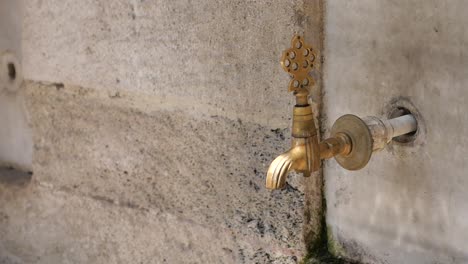 close-up of a water fountain with a brass tap in a stone wall