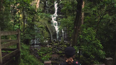 A-beautiful-young-woman-lookiung-at-a-jungle-waterfall-at-a-rocky-wall-in-the-deep-rainforest-jungle-in-Rincon-de-la-Vieja,-Costa-Rica