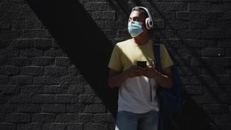mixed race man wearing face mask and using smartphone in the street