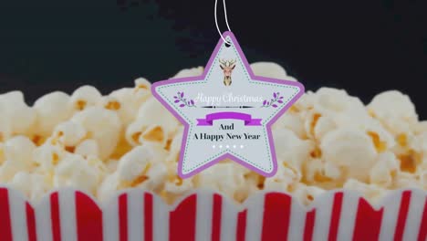 animation of christmas greetings on tag over popcorn on black background