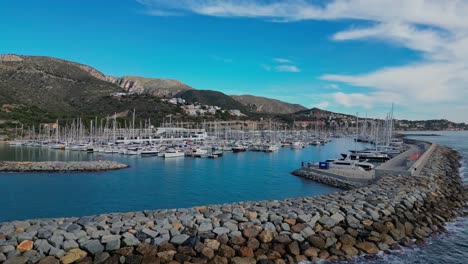 Veleros-Atracados-En-El-Puerto-De-Ginesta-Con-Montañas-Al-Fondo-Bajo-Un-Cielo-Azul-Brillante