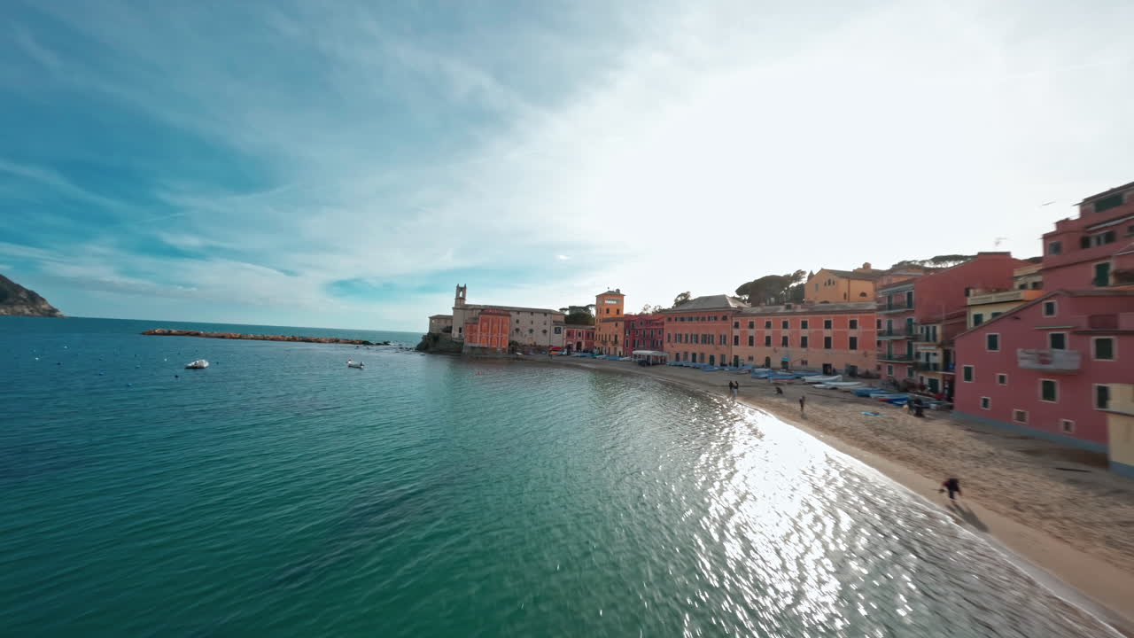 Edifici colorati sul lungomare che si snodano lungo una soleggiata costa marittima, visti da un drone FPV