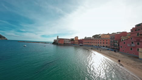 Colorful-beachfront-buildings-curve-along-a-sunny-seaside-shore-seen-from-an-FPV-drone