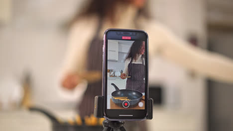 latin woman shooting video and cooking at the kitchen for share on blog