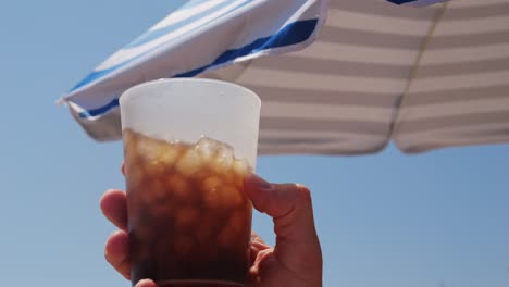 hand holding a cold drink under a beach umbrella